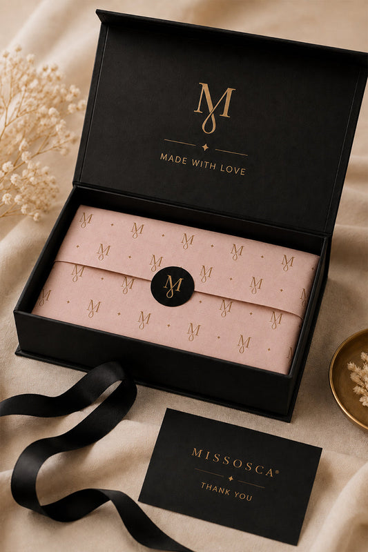 Open Missosca magnetic gift box with blush pink branded tissue paper, black ribbon and a thank-you card on a soft neutral background