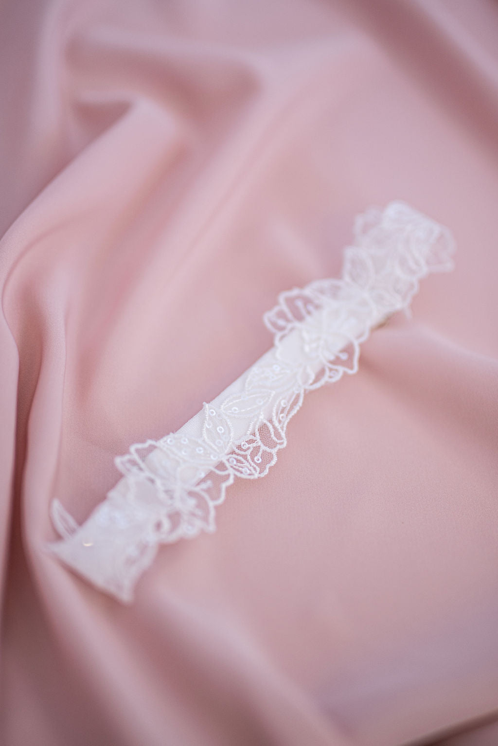 White lace and sequin wedding garter styled on soft pink bridal fabric.