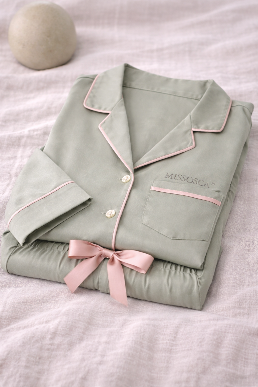 Folded sage green TENCEL™ lyocell pyjama set with blush trim neatly presented flat lay
