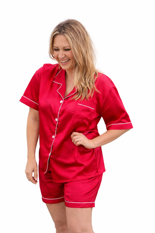 Woman wearing cherry red satin pyjama set with white contrast piping on a plain studio background