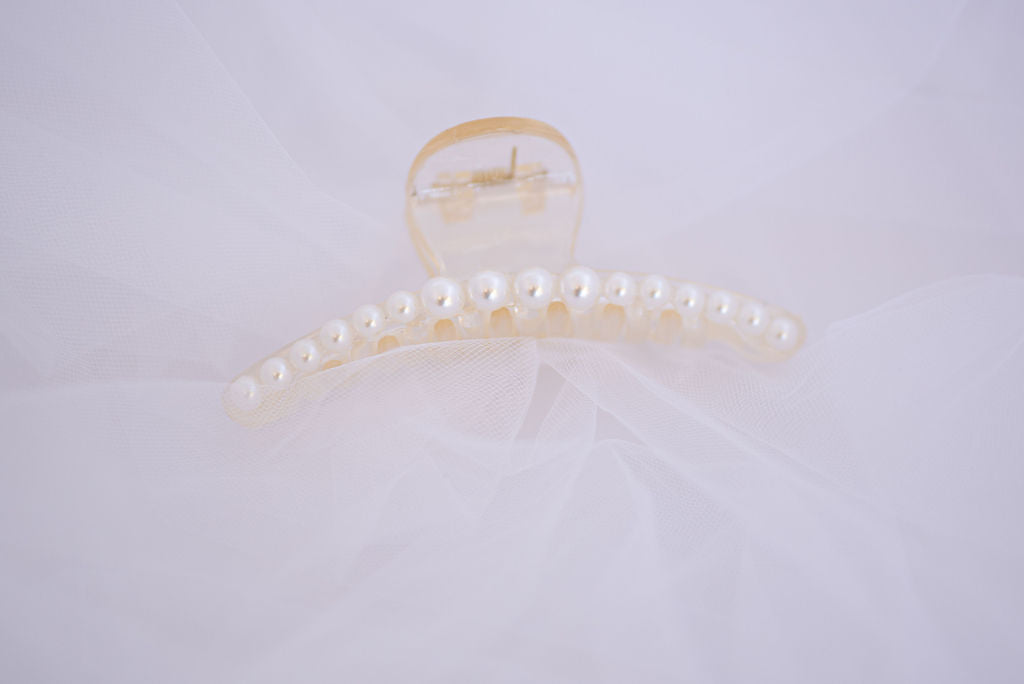 Faux pearl hair clip styled on textured fabric, classic bridal hair accessory detail.