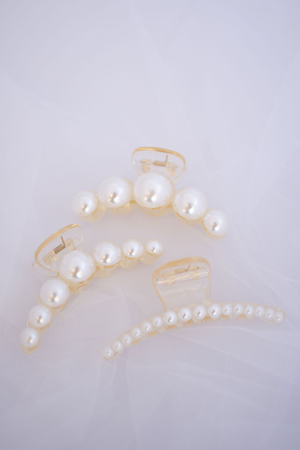 Curved faux pearl hair clip displayed on soft neutral background, elegant bridal hair accessory.
