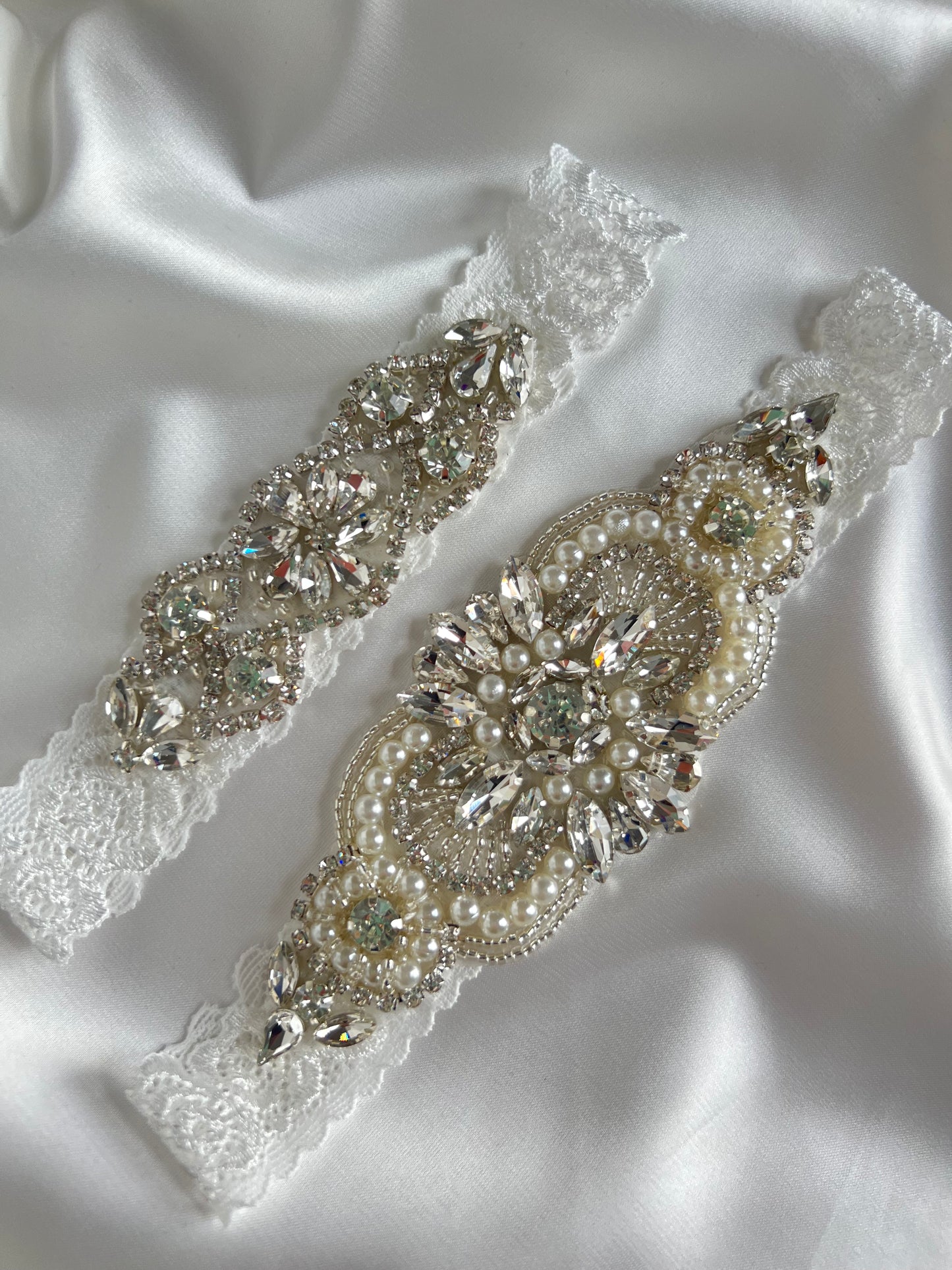 Pearl and diamante lace bridal garter set styled on soft satin fabric for elegant wedding presentation.