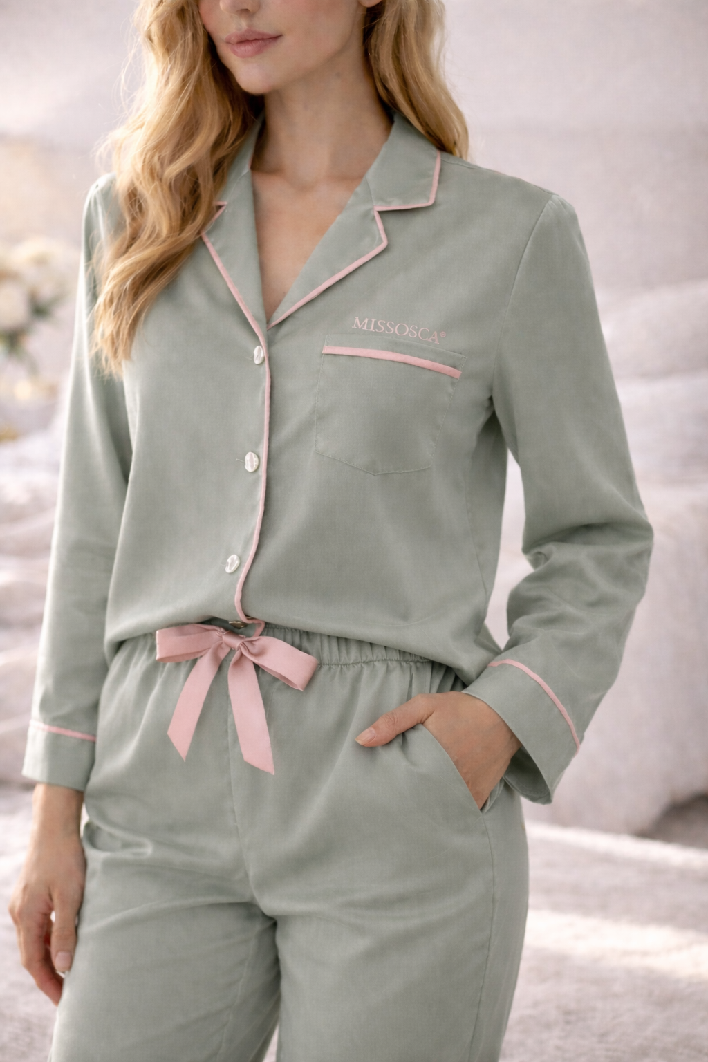 Sage green women’s luxury sleepwear set with pink piping styled in soft bedroom setting
