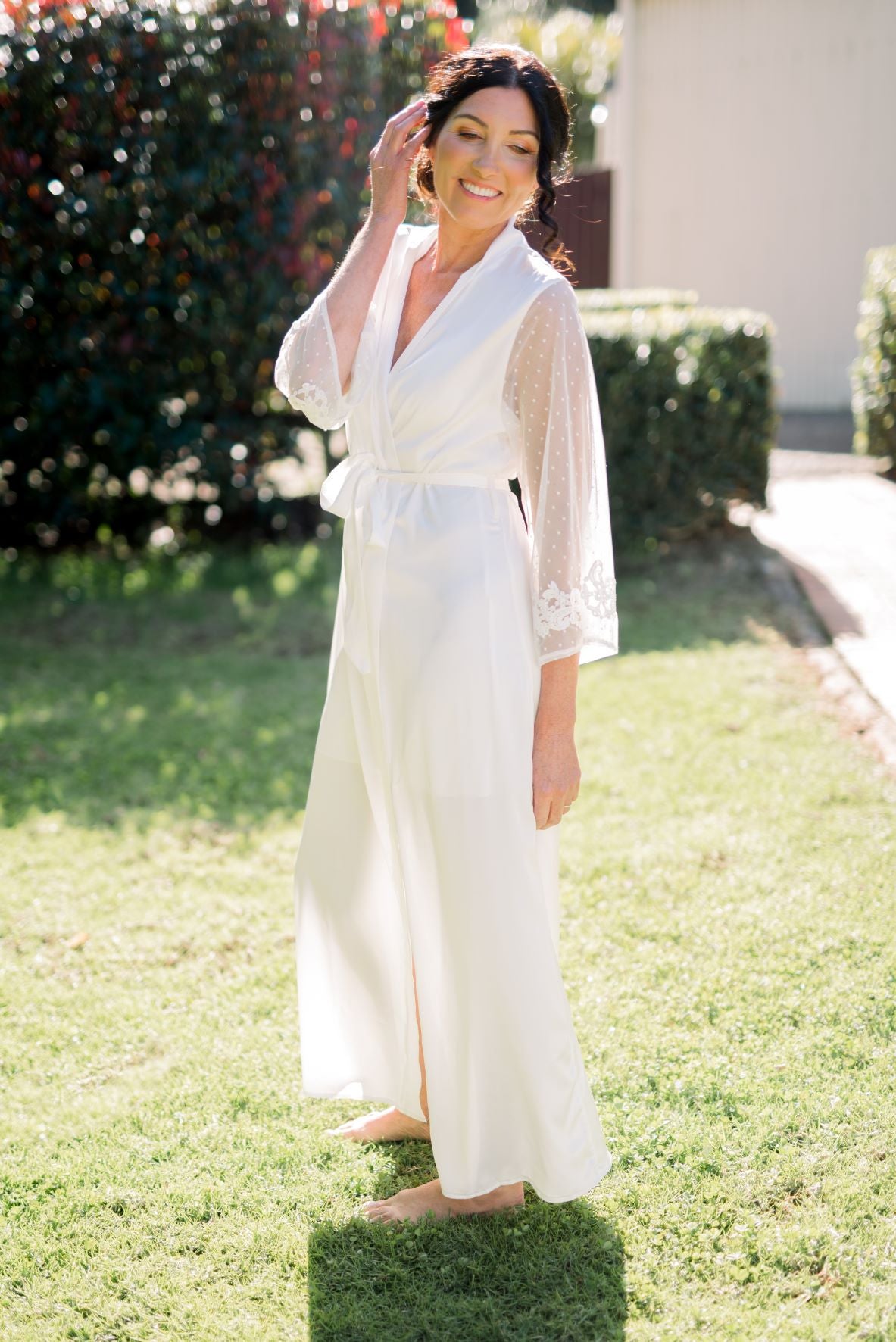 Bride wearing Ava lace sleeve satin robe during wedding getting ready photos outdoor garden